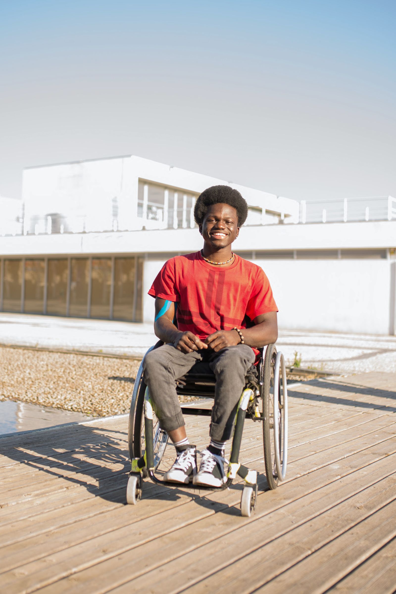 A young man smiling outdoors in his wheelchair.