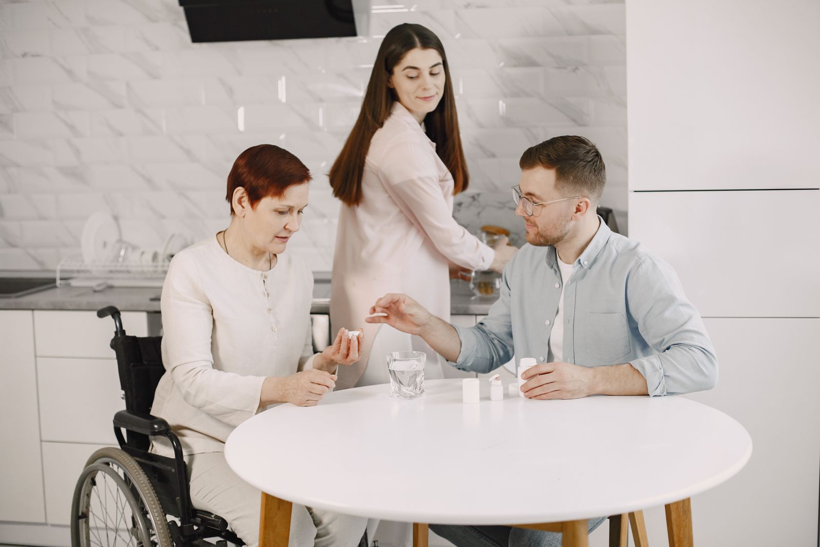 A carer helping a couple with medication at the kitchen table.