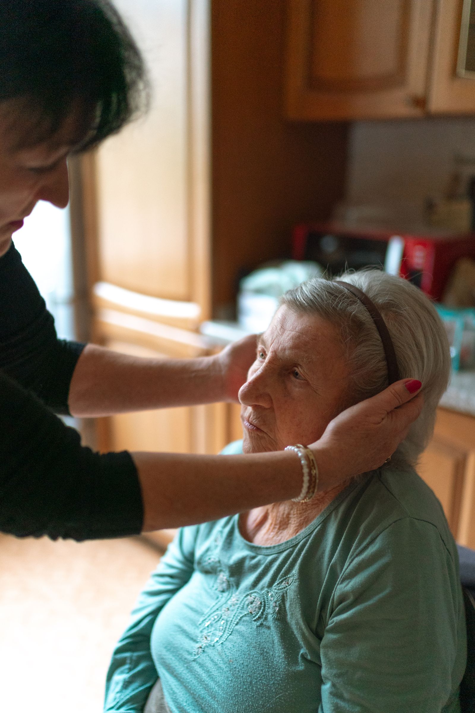 A carer gently helping an older woman with her hair at home.